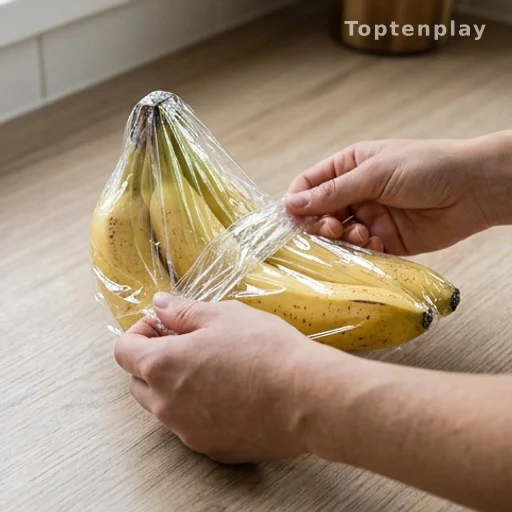 Mains enveloppant la tige d'un régime de bananes avec du film alimentaire